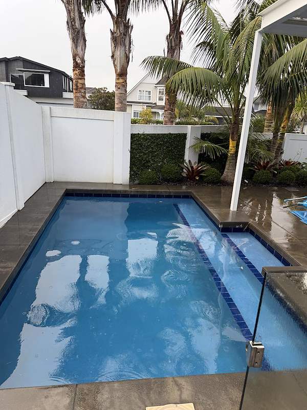 Rectangular pool with a raised spa, blue tiled edge, and white privacy fencing