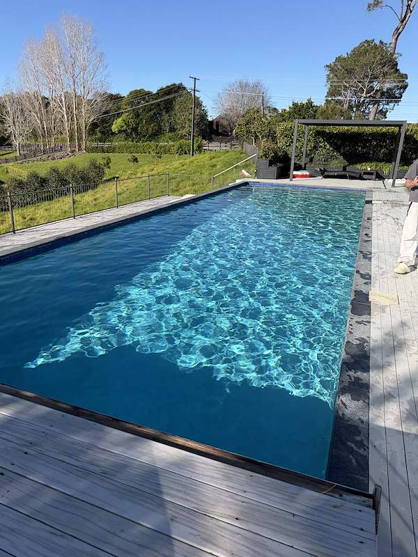 Long lap pool with a timber deck and pergola overlooking open countryside