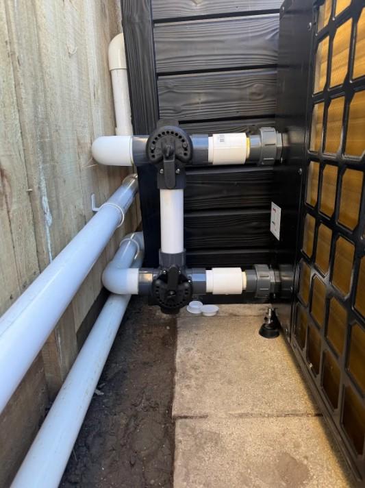 Heat pump bypass valve plumbed into a pool's pipework alongside the fence line